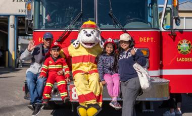 A family of four poses with Sparky in front of a Firetruck