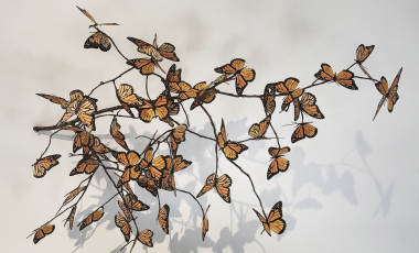 Paper monarch butterflies attached to a branch hanging on a white wall.
