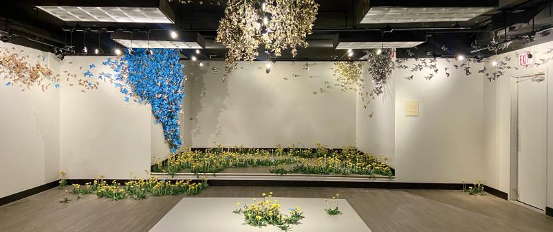 Wide view of the art gallery with paper butterflies hanging from the ceiling and paper dandelions on the floor.