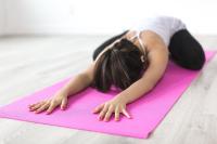 A woman face-down on a pink yoga mat with her arms stretched above her head.