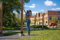 Mother and Baby standing in park touching Peace Poles with Arts & Learning Campus in the background