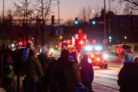 Santa standing in fire truck driving down road with crowd of people
