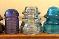 A line up of seven porcelain and glass insulators from telephone poles.