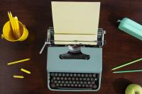 grey typewriter with yellow pencils and a green apple on a desk