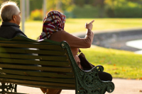 A photo from behind with two photos seated in front of a bench, pointing towards a green space in front of them