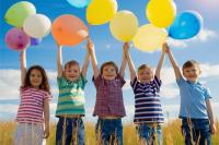Five children in a field holding balloons above their heads.