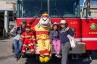 A family of four poses with Sparky in front of a Firetruck