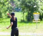 woman throwing a frisbee at a disc golf net in a park
