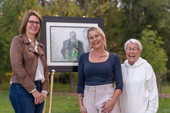 The mayor, Marg cox and Tanya stand in front of a portrait of former Mayor Bill