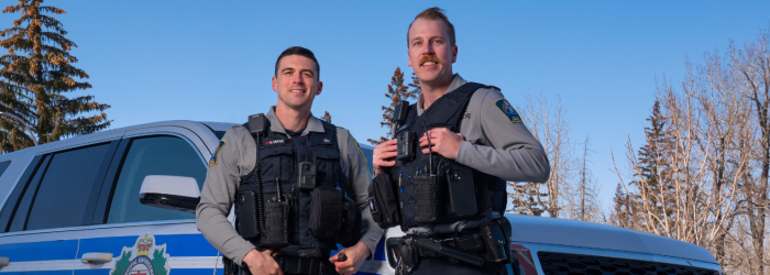 Two Okotoks municipal enforcement officers pose in front of police cruiser