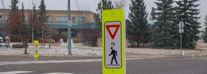 A sign in a cross walk remidning drivers to slow down