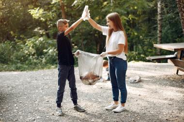 kids high fiving in a wooded area while picking up litter with white garbage bag
