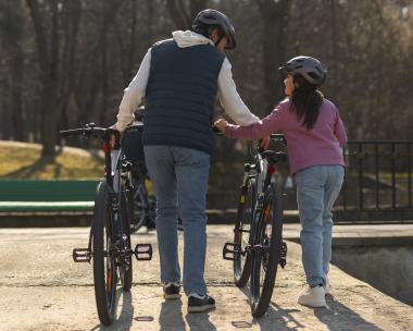 Dad and daughter holding up bikes, wearing bike helmets and walking together 