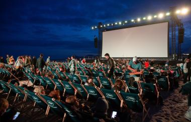 Outdoor movie screen with dark background and rows of people looking at the screen
