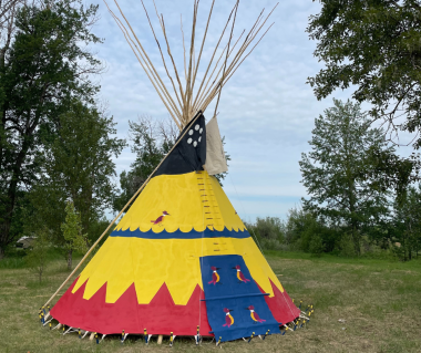 Town of Okotoks yellow, red and blue tipi sitting in a grassy area