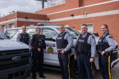 Members of Okotoks Municipal Enforcement and RCMP stand in front of a police car