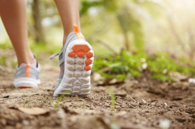 person walking on dirt wearing white and orange running shoes 