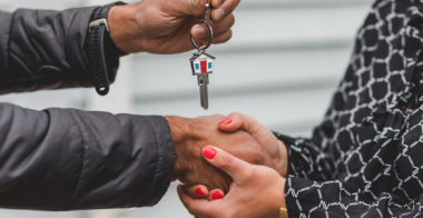 A close up of two people shaking hands while house keys are being passed over