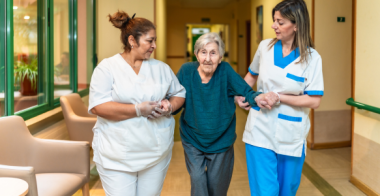 two health practitioners are supporting a senior who is walking 
