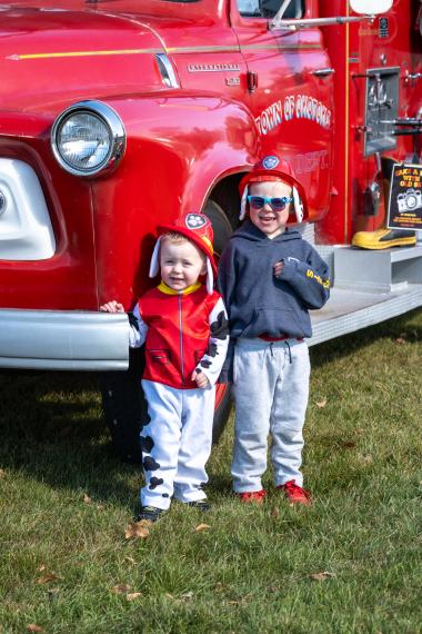 Two small kids stand in front of a firetruck